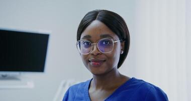 Young woman doctor of african american appearance without mask smiling looking directly at the camera in a modern bright clinic video