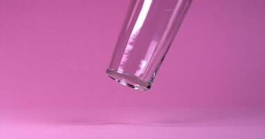 Glass falls and does not break, bouncing and turning over against a solid bright background in slow motion video