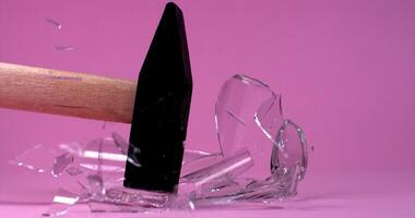 A hammer breaks a glass lying on a plain bright background, the fragments fly in different directions in slow motion video