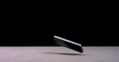 The mobile phone falls, bouncing off the surface, and is admitted to the screen. Small cracks appear on the screen. Slow motion on a black background video