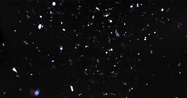 shiny confetti falling and scattering on black background in slow motion video