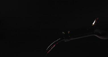 Red wine pouring from a bottle close-up, slow motion on a black background video