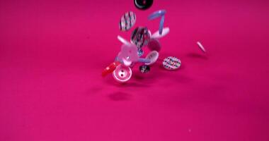Multi-colored buttons of different shapes fall on a pink background, in slow motion video