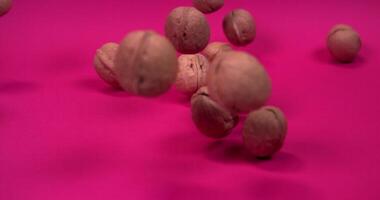Whole walnuts fall and bounce off the surface scatter to the sides, slow motion on a pink background video