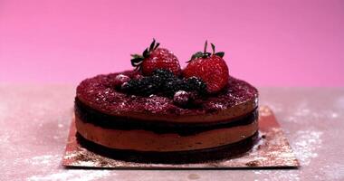 Powdered sugar slowly falling like snow covers a chocolate cake decorated with berries, in slow motion video