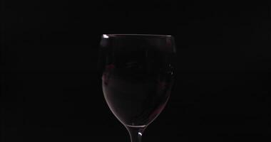 rojo vino reluce en un vaso, creando hermosa ondas, lento movimiento en un negro antecedentes video