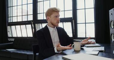 Young businessman in a business jacket communicates on a call with colleagues while working in a modern office. Business conversation in front of computer monitor video