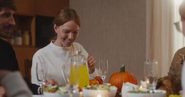 Beautiful young red-haired woman passes a plate of salad to the other end of the table, smiling and chatting with her family at the festive table video