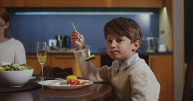 Handsome boy of European appearance eats a cucumber, impaled on a fork, sitting at a festive table with his family, celebrating Thanksgiving video