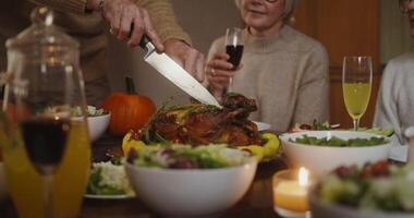 The father of the family cuts the turkey and distributes a piece to everyone, fun communication at the festive table, during the Thanksgiving Day celebration, close-up video