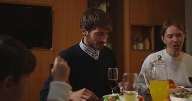 A beautiful family of European appearance is eating a festive dinner, sitting at a richly set table and happily talking to each other, celebrating Thanksgiving Day. video