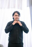 Dressing up , Man prepares for event in all black attire at window photo