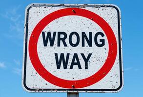 Weathered Wrong Way Sign, isolated on Clear Blue Sky, Symbolizing Error or Misdirection, Mistake and Misstep photo