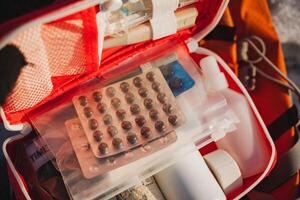 A compact red and white first aid kit that is stocked with various essential pills and bottles for health emergencies, ensuring you are prepared for any situation that may arise photo