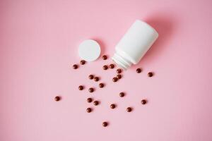 A white bottle filled with various pills is shown pouring them out onto a vibrant pink background, creating a striking visual appeal that highlights the pharmaceutical products inside photo