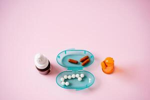 A bright blue container overflowing with assorted pills and a medication bottle creates a striking visual contrast against a bold pink background, capturing attention instantly photo