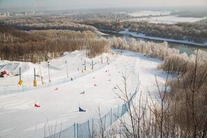A picturesque snowy ski slope, with a winding river gracefully flowing through the background, creating a stunning contrast to the winter wonderland surrounding the area photo
