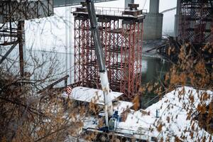 A large crane is currently being used for the construction of a bridge that spans over a river, showcasing engineering excellence and skillful planning in infrastructure development photo