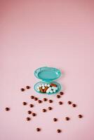 A blue container overflows with colorful pills and chocolate balls, creating a striking contrast against a soft pink background, enhancing its visual appeal and attracting attention photo