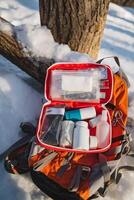 A large backpack that is fully packed with a wide array of essential first aid supplies remains unused and untouched, lying silently in the cold snow, waiting for someone to find it photo