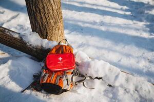 A vibrant outdoor winter scene prominently features a backpack and a first aid kit positioned in breathtaking snowy terrain, showcasing the beauty of nature in winter photo