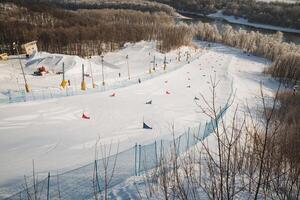A picturesque snowy ski slope is adorned with a bright blue fence, and majestic trees can be seen in the beautiful background, creating a perfect winter scene for skiers and snowboarders photo