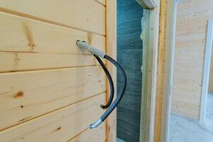 A black electrical wire is hanging loosely from a wooden wall, which is likely constructed from planks of hardwood or plywood, and it may have received a wood stain or finish for protection photo