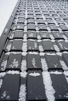 This is a detailed closeup view of a roof that is capped with a layer of fresh snow, highlighting its texture and the serene beauty of winter. The snow reflects a gentle light photo