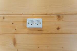 A white electrical outlet is securely mounted on a wooden wall, blending functionality and elegance, merging modern technology with classic style for an inviting ambiance photo