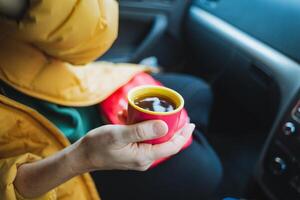 A person is comfortably seated inside a car while holding a steaming cup of tea in their hand, relishing and savoring the warmth and delightful flavor that it provides during their drive photo