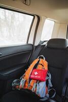 Inside the back seat of a car, there is a backpack along with a first aid kit positioned safely in case of emergencies or travel needs. These items are important for preparedness photo