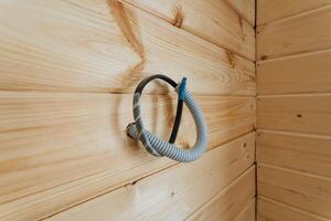 A garden hose is hanging down on a beautifully finished wooden wall, showcasing the rich texture and color of the woods surface, adding character to the surrounding area photo