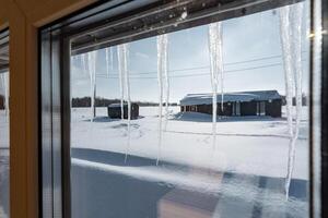 Icicles elegantly dangle from the window, creating a stunning view of an expansive snowcovered field blanketed in pristine, untouched white snow as far as the eye can see photo