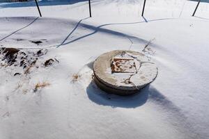 A heavy and durable concrete manhole cover is currently sitting out in the deep, soft snow that has fallen all around it this winter season, creating a picturesque and cold scene photo
