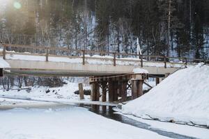 A picturesque bridge spans across a snowy river, with tall trees in the background, creating a serene winter landscape that captures the essence of the cold season perfectly photo