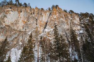 A majestic snowcapped mountain rises into the clear blue sky, surrounded by lush trees and a steep cliff, showcasing the exquisite beauty of nature in this serene setting photo