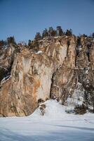In a picturesque, snowy field, an impressive and large rock formation captivates viewers, standing out dramatically against the serene and pristine white winter landscape that surrounds it photo
