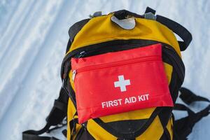 A bright yellow backpack featuring a prominently placed red first aid kit attached to it, making it easily visible and prepared for any emergency situations that might arise photo