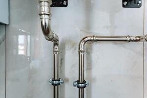 Two stainless steel pipes are connected to one another securely on the surface of a tiled wall, showcasing a common plumbing installation found in household applications photo