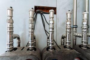 Shiny, polished stainless steel pipes are securely fixed to a sturdy wall, highlighting their robust design, versatility, and vital role in plumbing and engineering applications photo