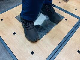 A person wearing black shoes is standing firmly on a polished wooden floor, showcasing the contrast between the shoes and the natural wood grains beneath them, creating a striking visual photo