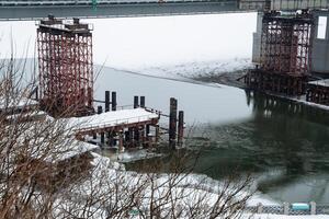 A bridge is currently under construction over a vast body of water, which could be a lake or a reservoir, showcasing impressive engineering in winter conditions with snow, mist, and fog photo