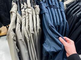 A person is holding a vibrant blue shirt in front of a wellorganized row of various shirts in a retail setting, showcasing fashion diversity and textile options to choose from photo