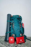 A vibrant green backpack, a bright red first aid kit, and a neatly rolledup yoga mat are all set and ready for adventure, combining both style and functionality for anyone who seeks it photo