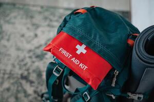 A very useful first aid kit is conveniently sitting on top of a sturdy backpack that is located next to a colorful yoga mat on the floor, ready for any emergencies or activities photo