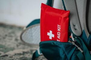 A bright red first aid kit is protruding from a backpack, making it easily visible and accessible in case of emergencies while on the go, ensuring safety during outdoor activities photo