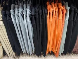 A bunch of various colored shirts are currently hanging neatly on a clothing rack for display, showcasing an array of vibrant hues and styles for potential buyers to admire photo