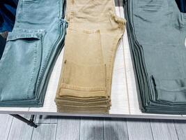 Situated on a table, there are three pairs of pants that have been neatly stacked one on top of the other. Each pair showcases unique features, adding versatility to the collection photo