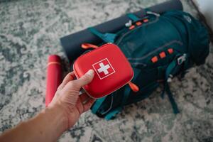 A person is holding a first aid kit in front of a backpack that seems ready for an outdoor adventure, emphasizing the importance of safety while engaging in various activities outdoors photo