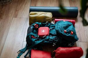 A red first aid kit is placed inside a backpack that is resting on a wooden floor, conveniently positioned beside a yoga mat, ready for use or emergency assistance when needed photo